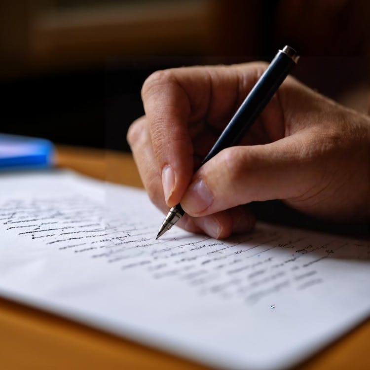 شخص يكتب على ورقة بقلم، مركزًا على عمله.